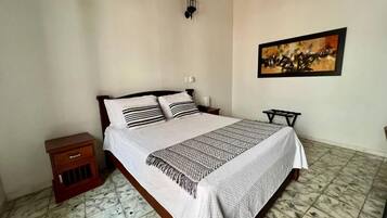 A bedroom with a bed, a nightstand, a wall-mounted lamp, and a framed picture.