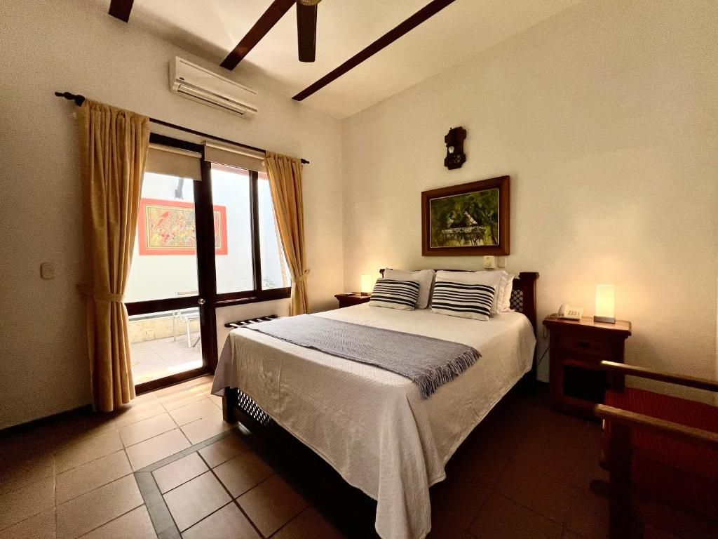 Una habitación de hotel con una cama, una mesita de noche, una lámpara, una ventana con cortinas y un cuadro en la pared.