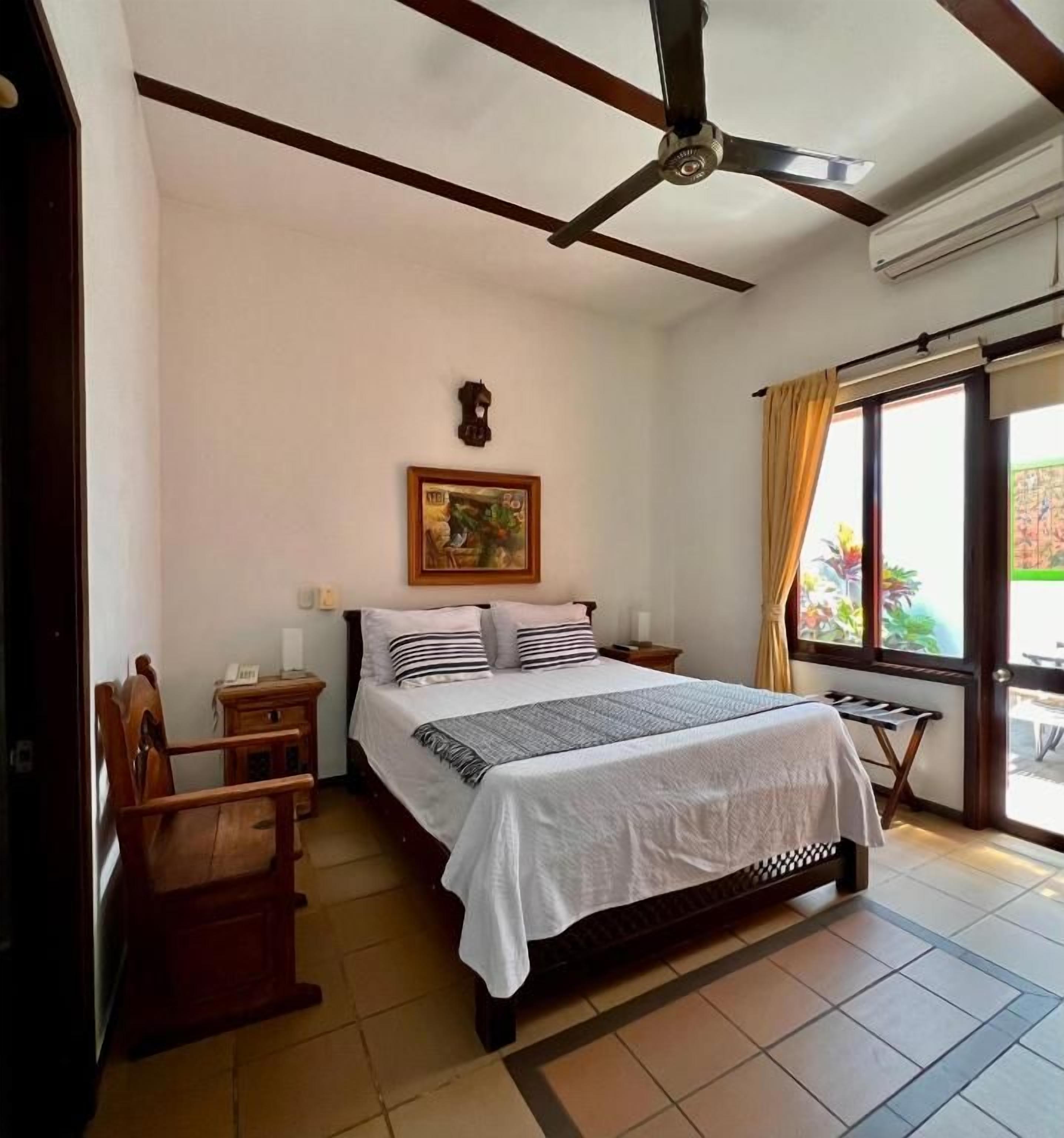 Un dormitorio con una cama, un ventilador de techo, una ventana con cortinas y un reloj en la pared.