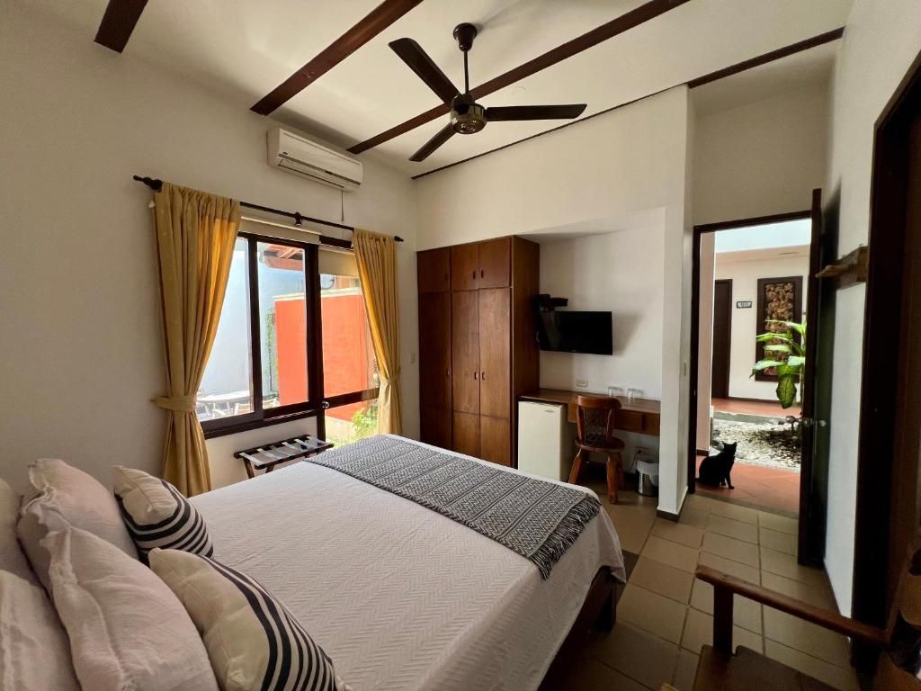 A bedroom with a bed, a desk, a television, and a ceiling fan.