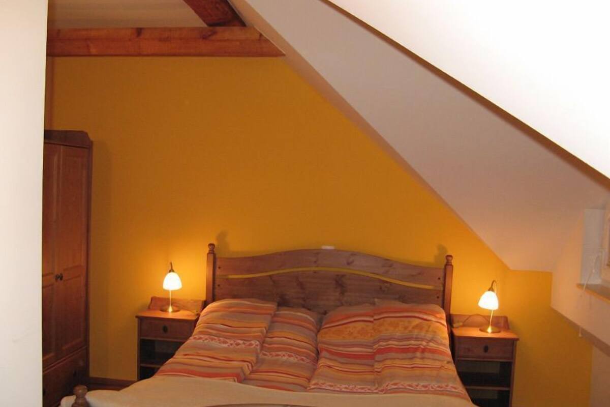 Une chambre avec un plafond en pente, une tête de lit en bois et deux lampes de chevet.