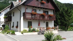 A two-story building with a balcony, a bicycle parked in front, and a mountain backdrop. - Apartments Bohinj na vasi (Bohinj)