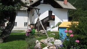 A house with a swing set, a small shed, and a garden with rocks and flowers. - Apartments Bohinj na vasi (Bohinj)