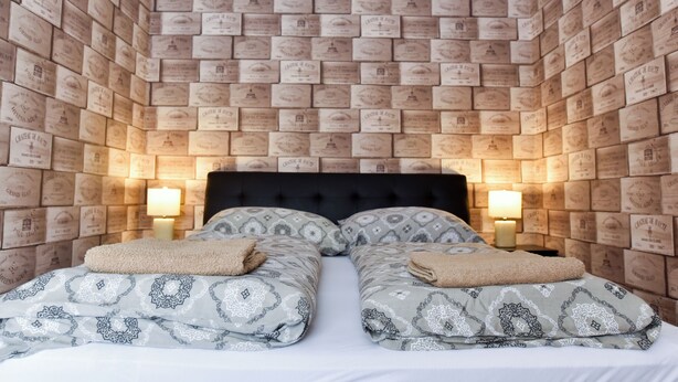 A room with a brick-patterned wall, a black upholstered headboard, two bedside tables with lamps, and patterned bedding. - Corvin Point Rooms and Apartments (Budapest)