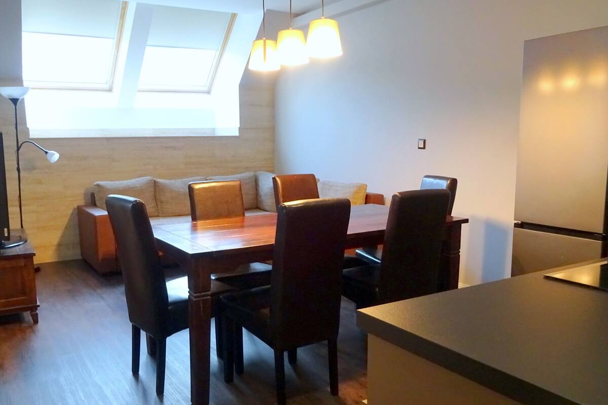 A modern kitchen with a dining area, wooden flooring, and a built-in oven.