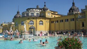 A public swimming pool with people swimming and relaxing, surrounded by a yellow building with classical architecture. - Corvin Point Rooms and Apartments (Budapest)