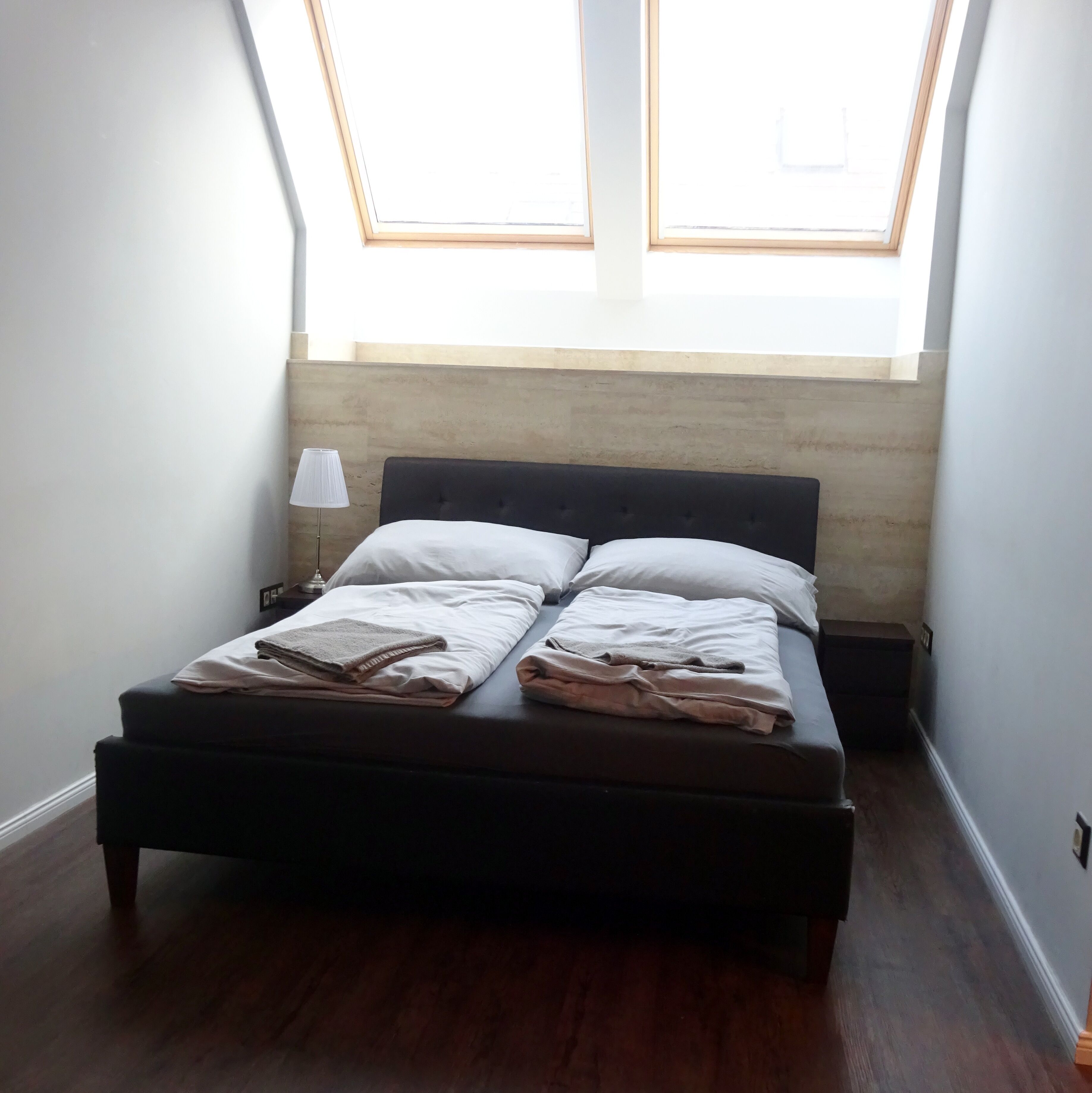 A bedroom with a bed, a nightstand, a lamp, and a skylight.