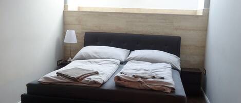 A bedroom with a bed, a nightstand, a lamp, and a skylight.
