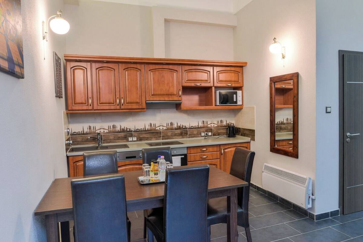 A compact kitchen with wooden cabinets, a dining table with chairs, a microwave, and a small TV on a stand.