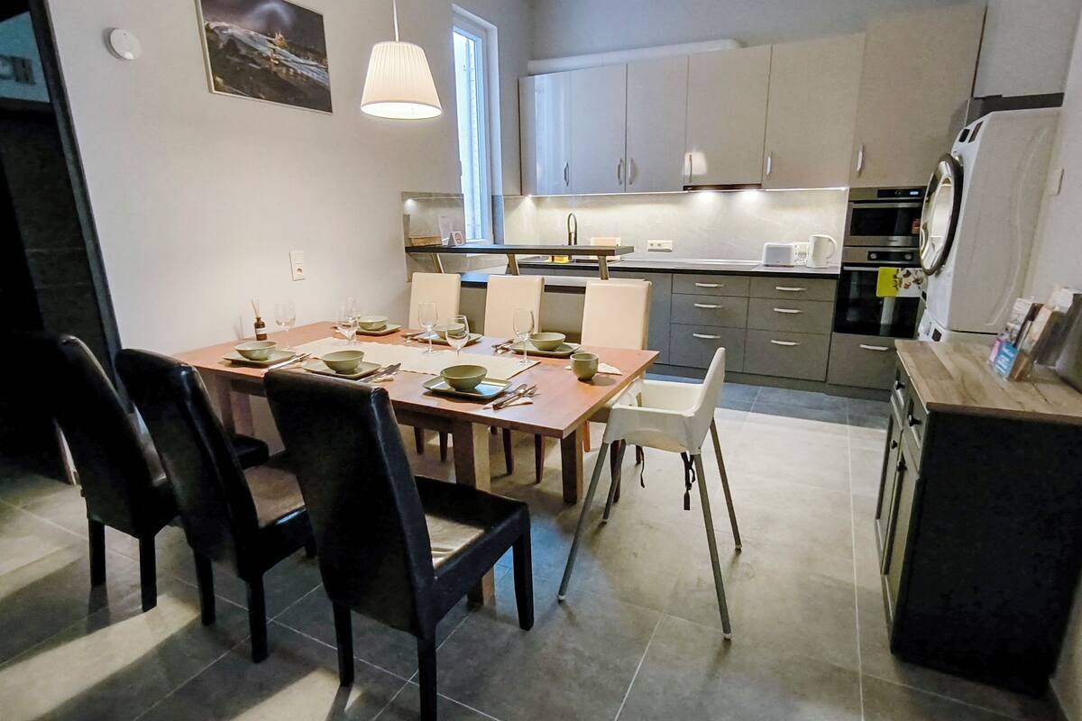 A modern kitchen with a dining area. It includes a table set for four, chairs, and a refrigerator.