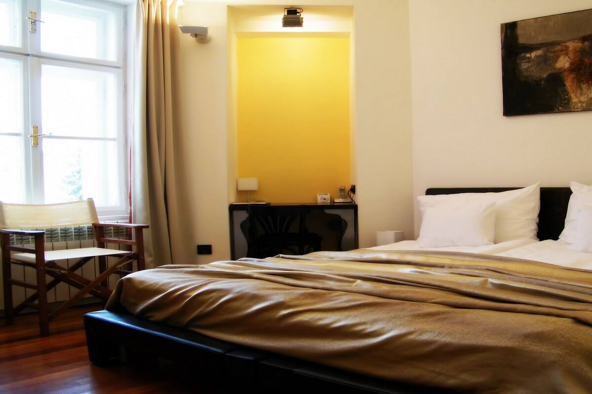 Hotellihuone, jossa on sänky, työpöytä, tuoli ja taulu seinällä.