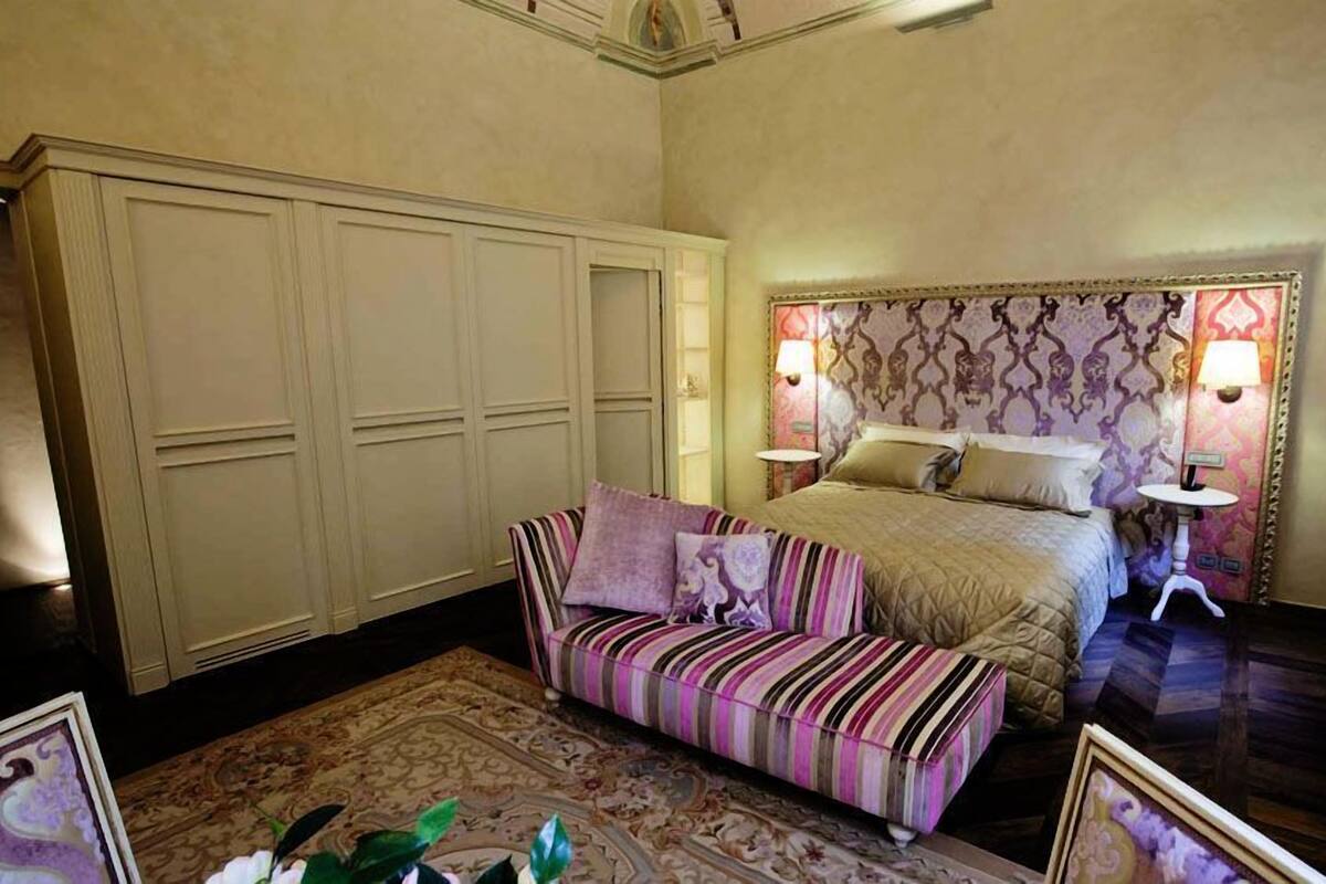 A bedroom with a large bed, a striped sofa, a wardrobe, and two bedside lamps.