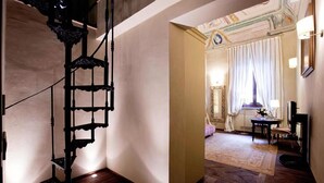 Een kamer met een spiraaltrap, een grote spiegel en uitzicht op een balkon met gordijnen.