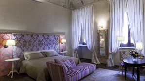 Een slaapkamer met een bed, een bank, een klein rond tafeltje, een stoel en een spiegel.