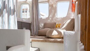 A sunlit interior with a staircase leading to a seating area, featuring a window and a life preserver hanging on the wall. - Glykeria Mini Suites (Santorini)