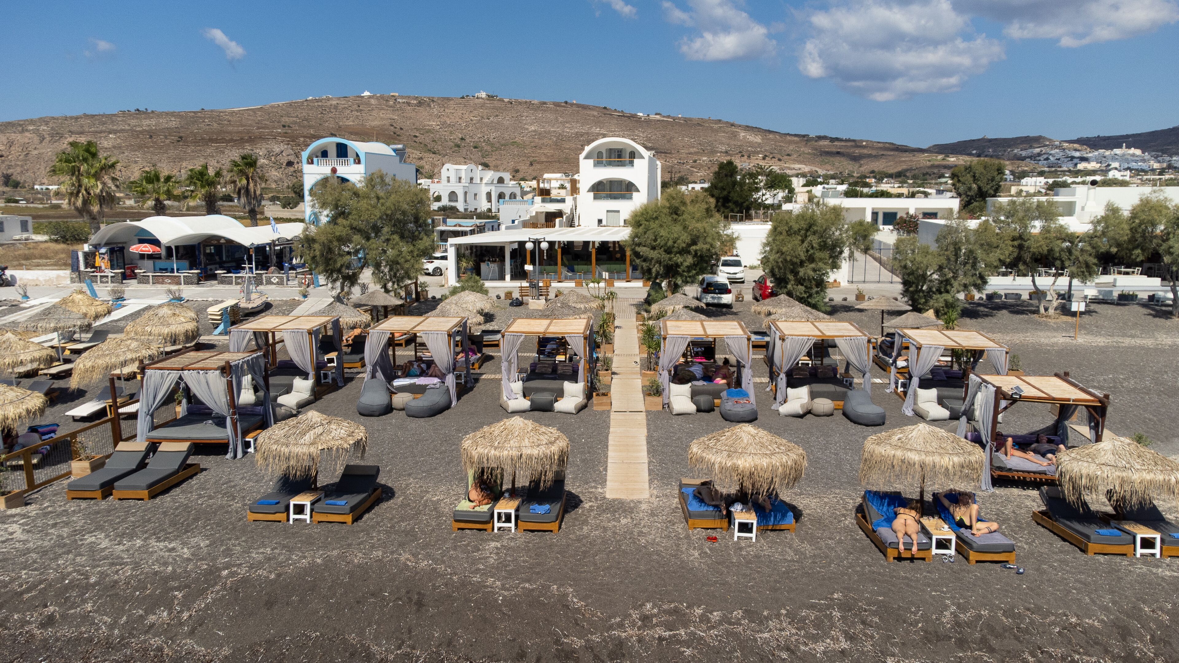A beachside resort with thatched-roof cabanas, sun loungers, and a white building with a dome.