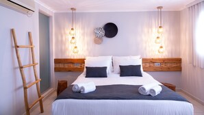A neatly arranged bedroom with a large bed, bedside tables, a wooden ladder, and wall-mounted lights. - Glykeria Mini Suites (Santorini)