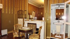 A room with a fireplace, a mirror, a sink, and two chairs. - Hôtel Windsor Home (Paris)