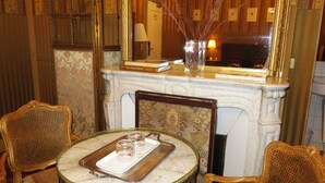 A room with a marble fireplace, a mirror, a tray with glasses, and two ornate chairs. - Hôtel Windsor Home (Paris)