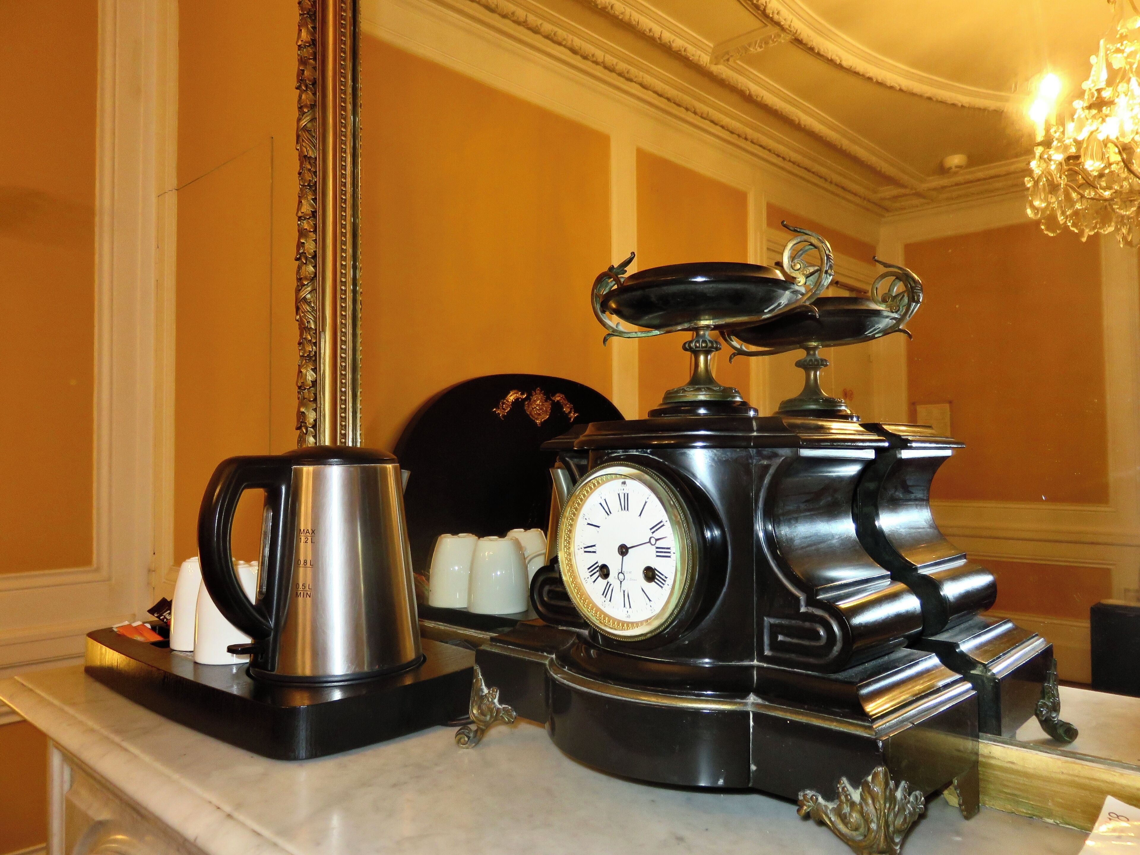 A vintage coffee maker with a clock, a coffee pot, and a teapot on a marble countertop.