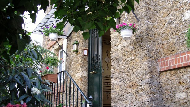 A stone building with a green door, a staircase, and hanging flower pots. - Hôtel Windsor Home (Paris)