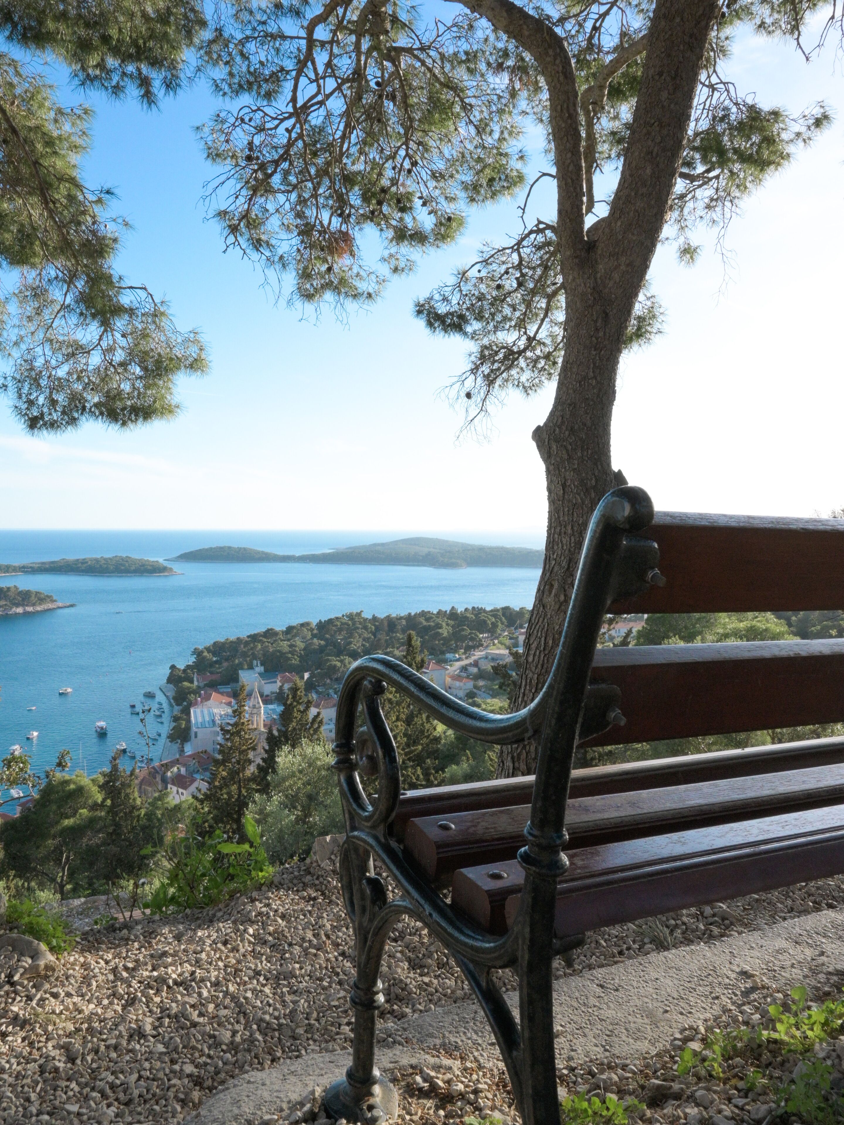 Un banc placé face à un paysage côtier, avec un ciel dégagé et une terre ferme visible au loin.