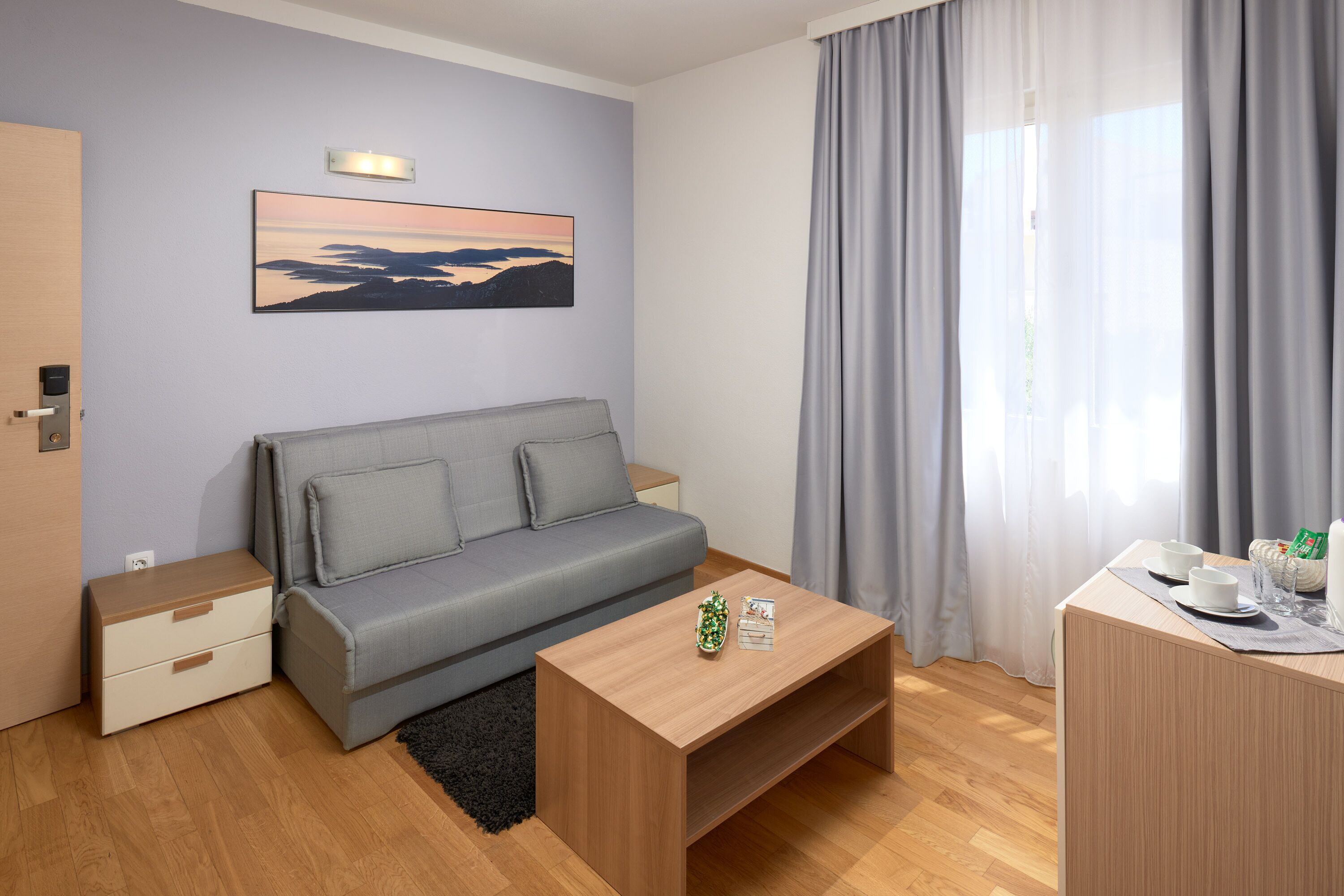 A modern room with a grey sofa, wooden coffee table, and a painting of a sunset.