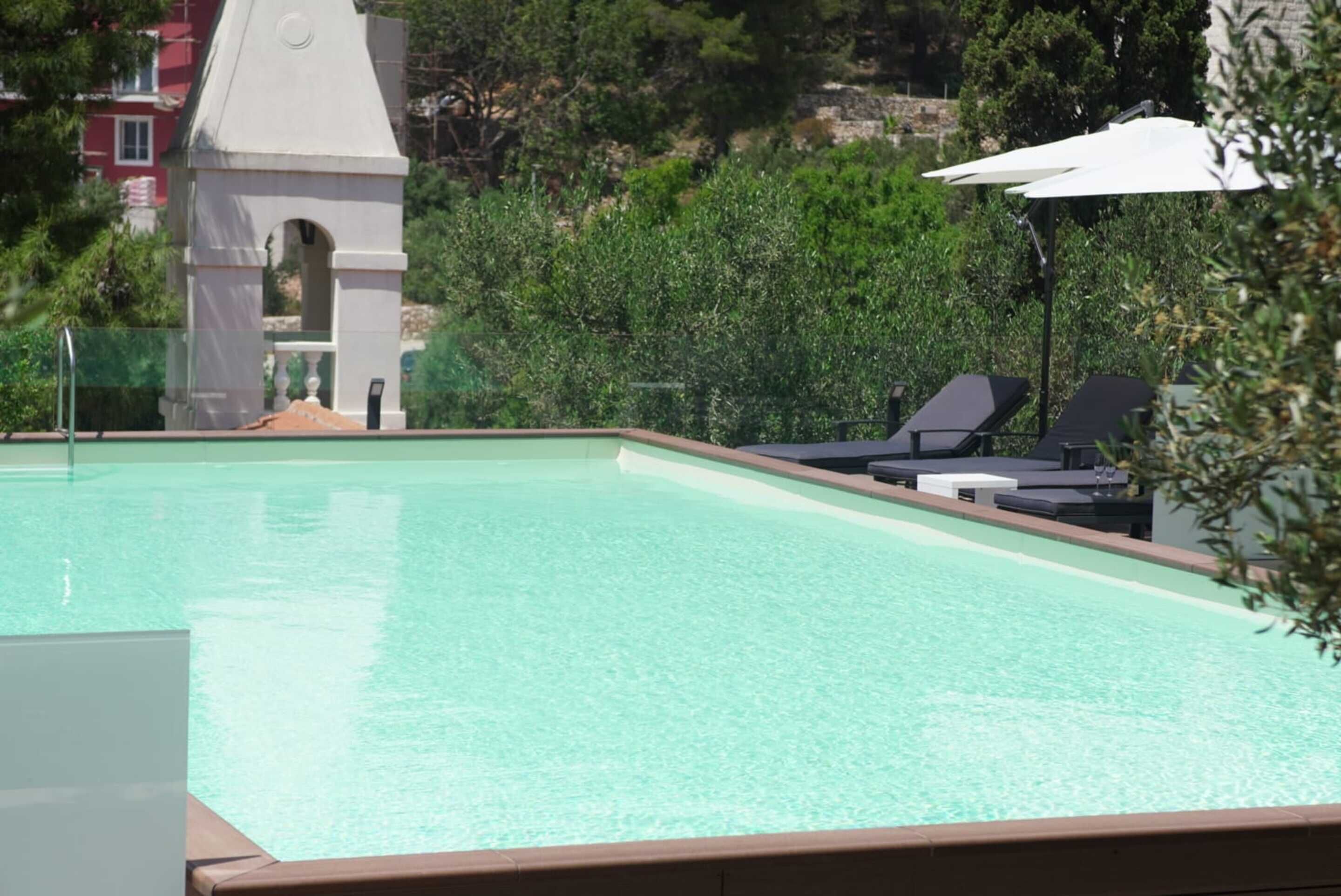 A swimming pool with lounge chairs and umbrellas, surrounded by greenery and a small tower structure.