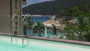 Ein Schwimmbecken mit einer Metallleiter, einer Leuchtturm-Dekoration und Blick auf Strand und Wald im Hintergrund.