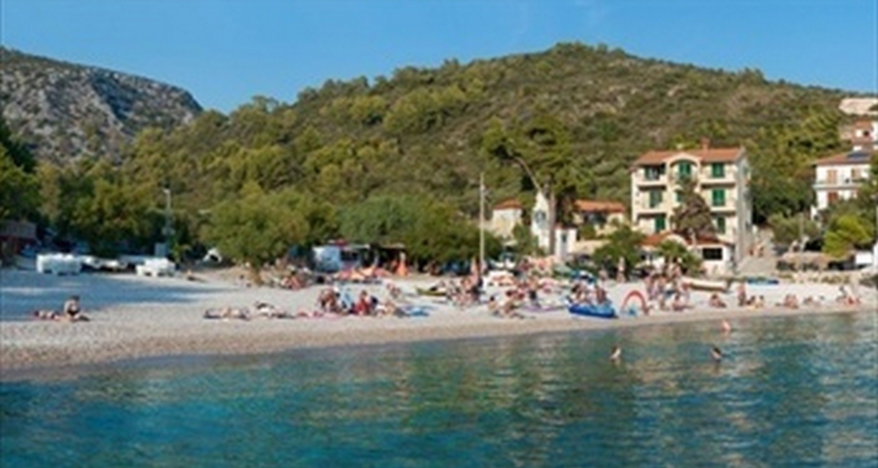 Ein Strand mit Gebäuden im Hintergrund, einem klaren Himmel und Menschen im Sand.