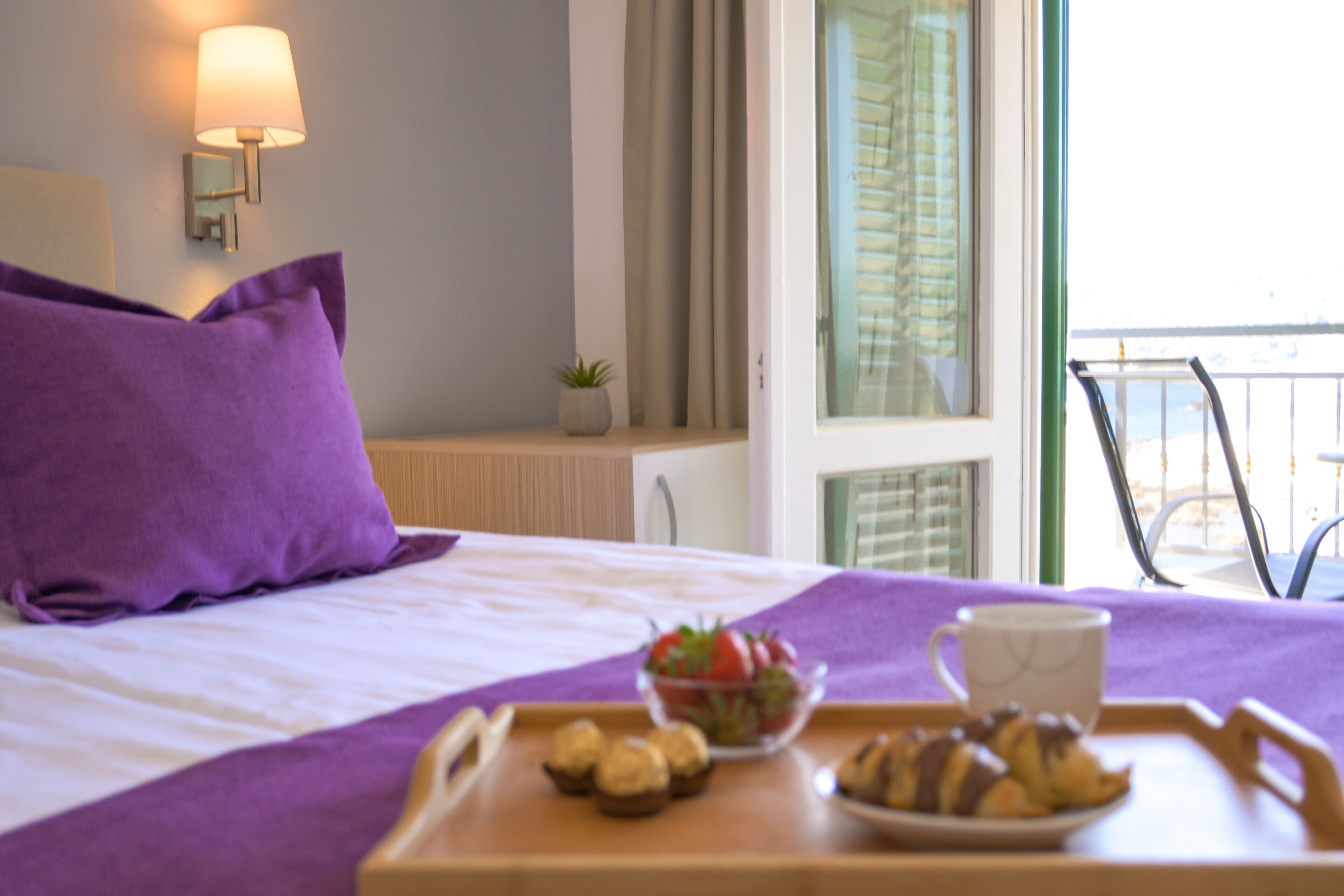 Een hotelkamer met een bed, een dienblad met gebak en een kom aardbeien, een lamp en een raam met gordijnen.