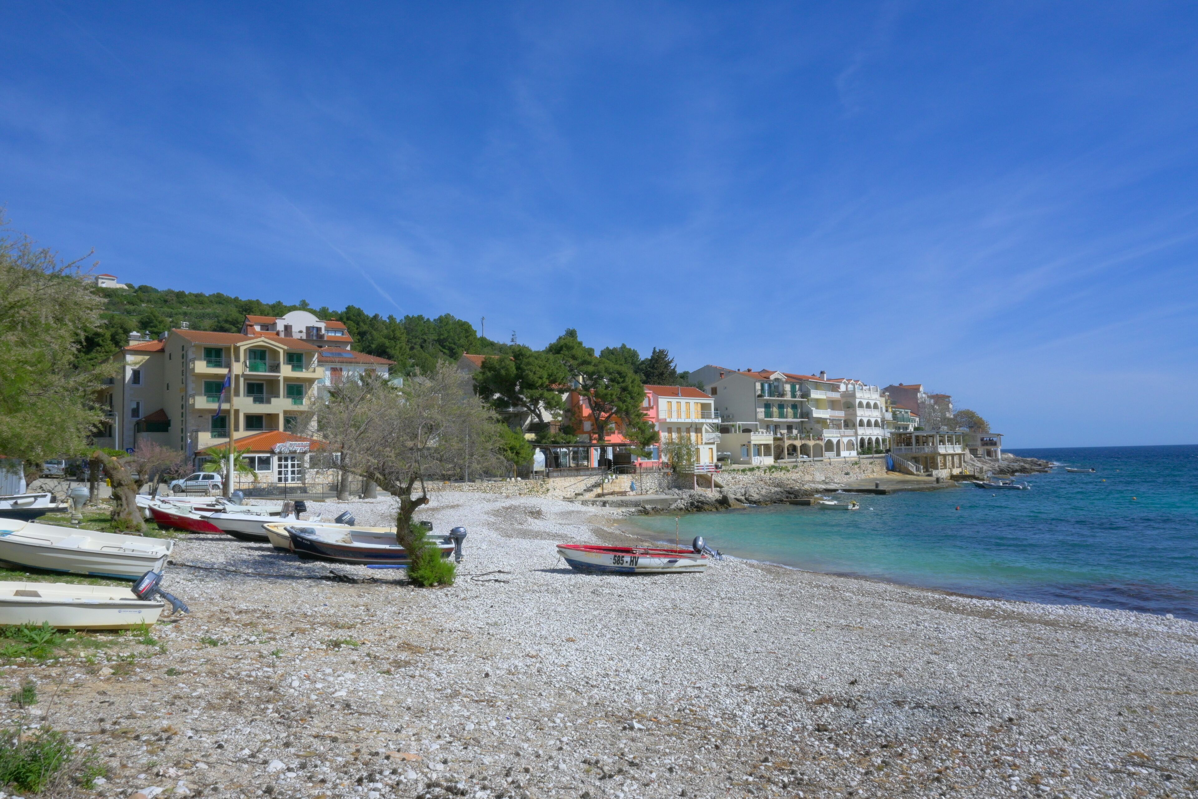 A pebbled beach with boats, buildings, and a clear blue sky.