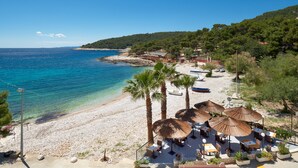 Ein Strandhotel mit Außenbestuhlung, Palmen und Meerblick.