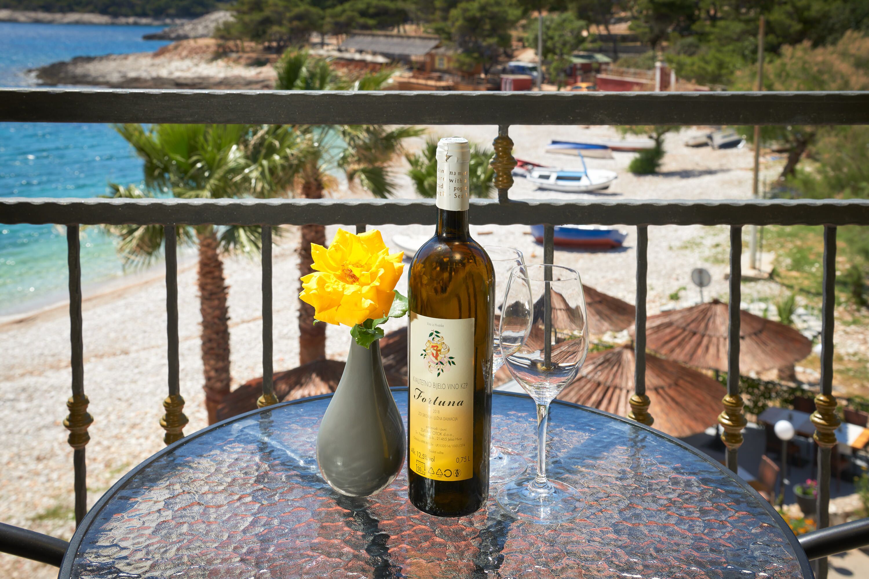A table with a bottle of wine, a glass, and a vase with a yellow flower.