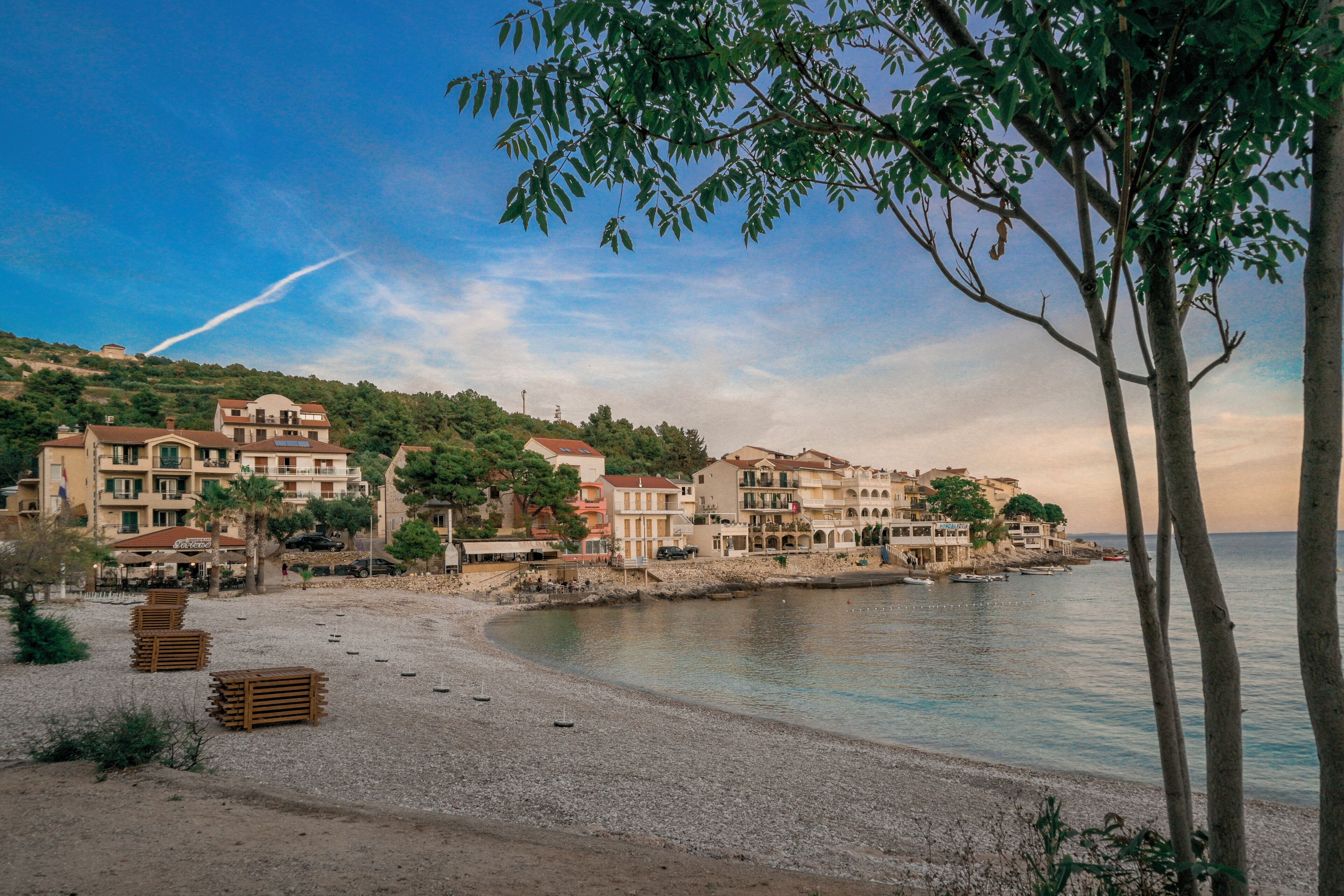 A coastal town with buildings along the shore, a pebbled beach, and a clear sky.