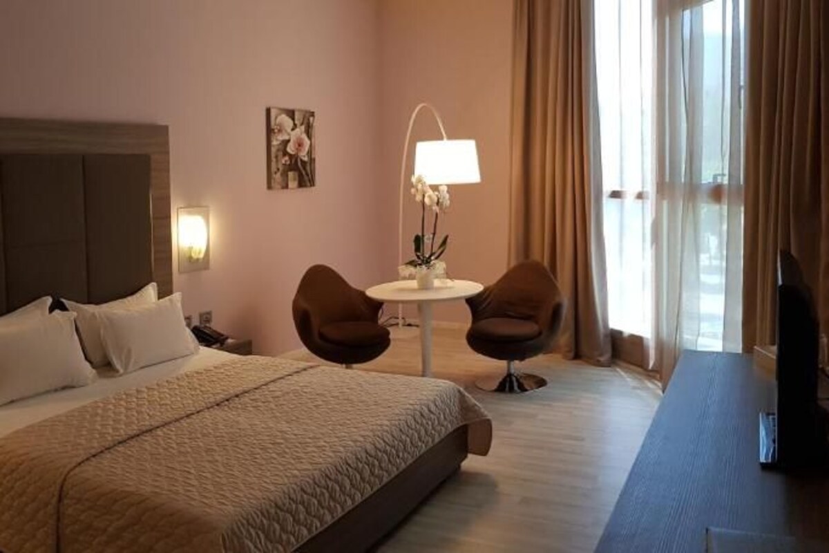 Une chambre d’hôtel avec un grand lit, deux fauteuils, une petite table et un téléviseur.
