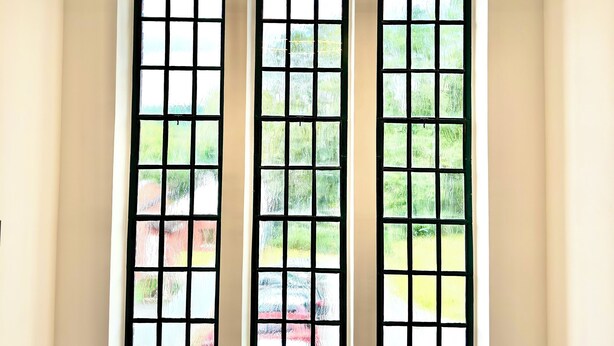 Ein Zimmer mit drei Fenstern, auf jedem Fensterbrett ein Blumentopf.