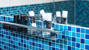 Baño con salpicadero de azulejos azules y repisa de vidrio con artículos de tocador.