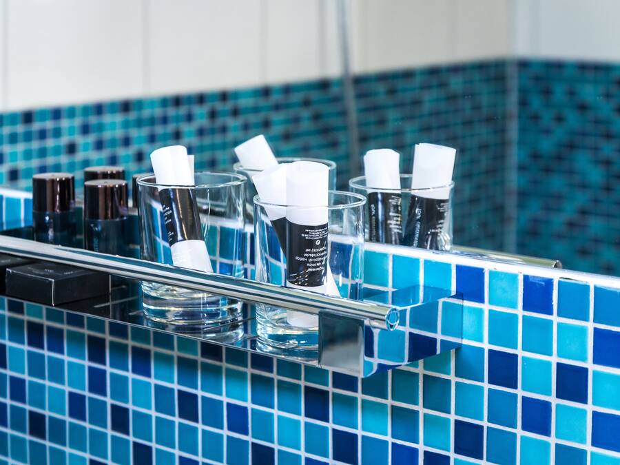 Baño con salpicadero de azulejos azules y repisa de vidrio con artículos de tocador.