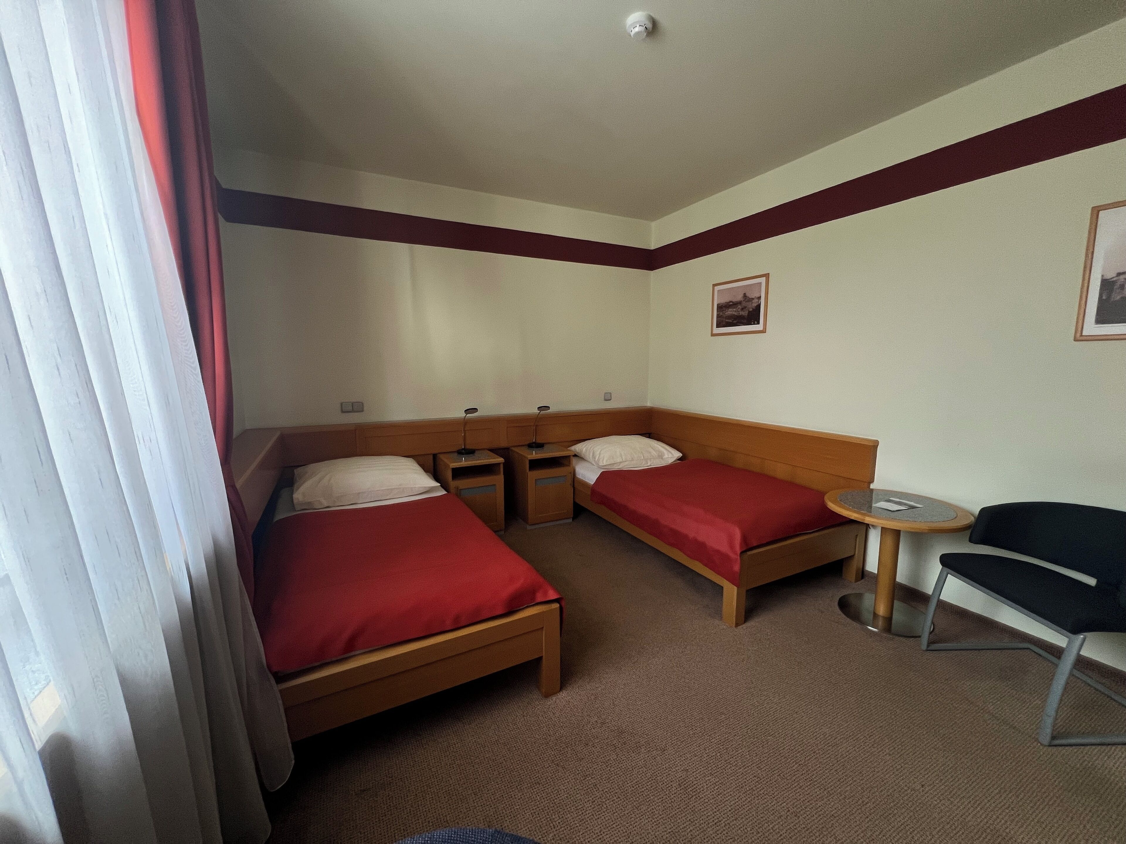 A hotel room with two single beds, a small table, a chair, and a picture on the wall.