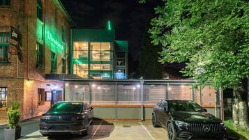A building with a neon sign, two parked cars, and a brick facade.