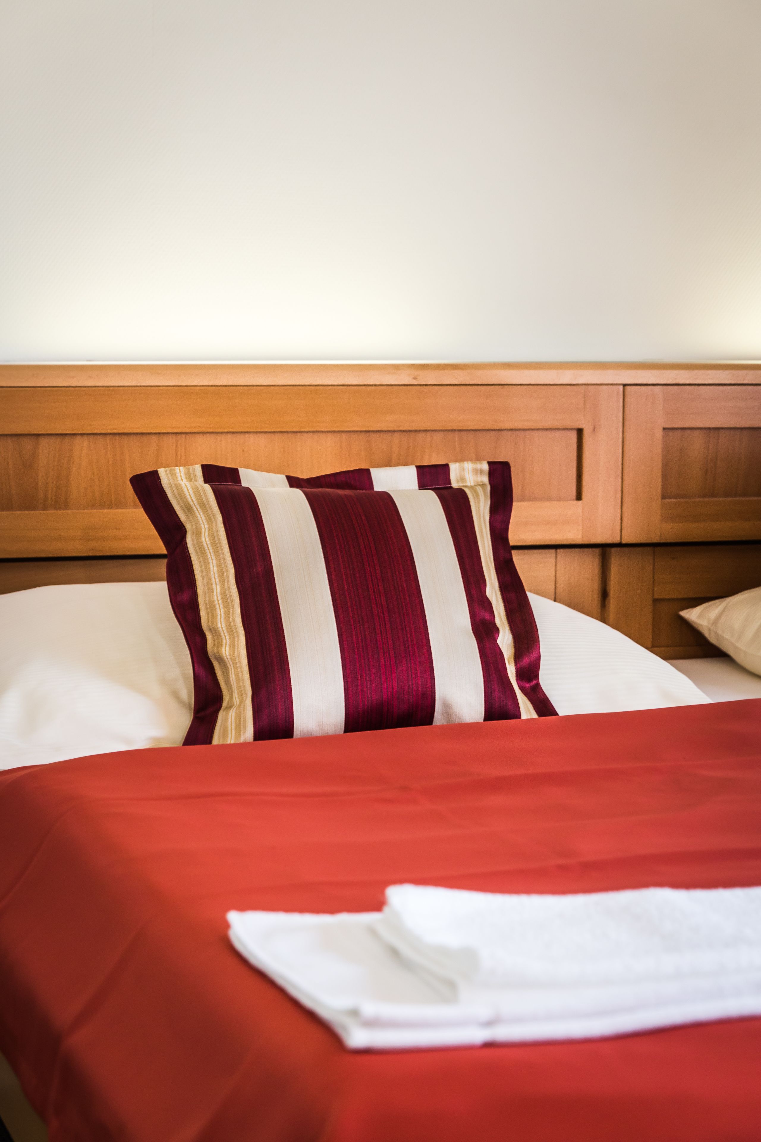 A neatly made bed with a red bedspread and a striped pillow.