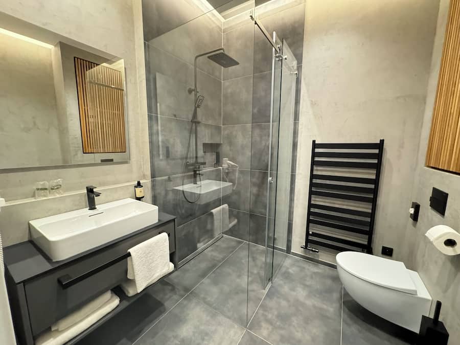 Un bagno moderno con doccia vetrata, lavandino bianco e mobile contenitore nero.