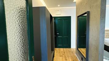 A hallway with wooden flooring, a green door, and a mirror on the right wall.