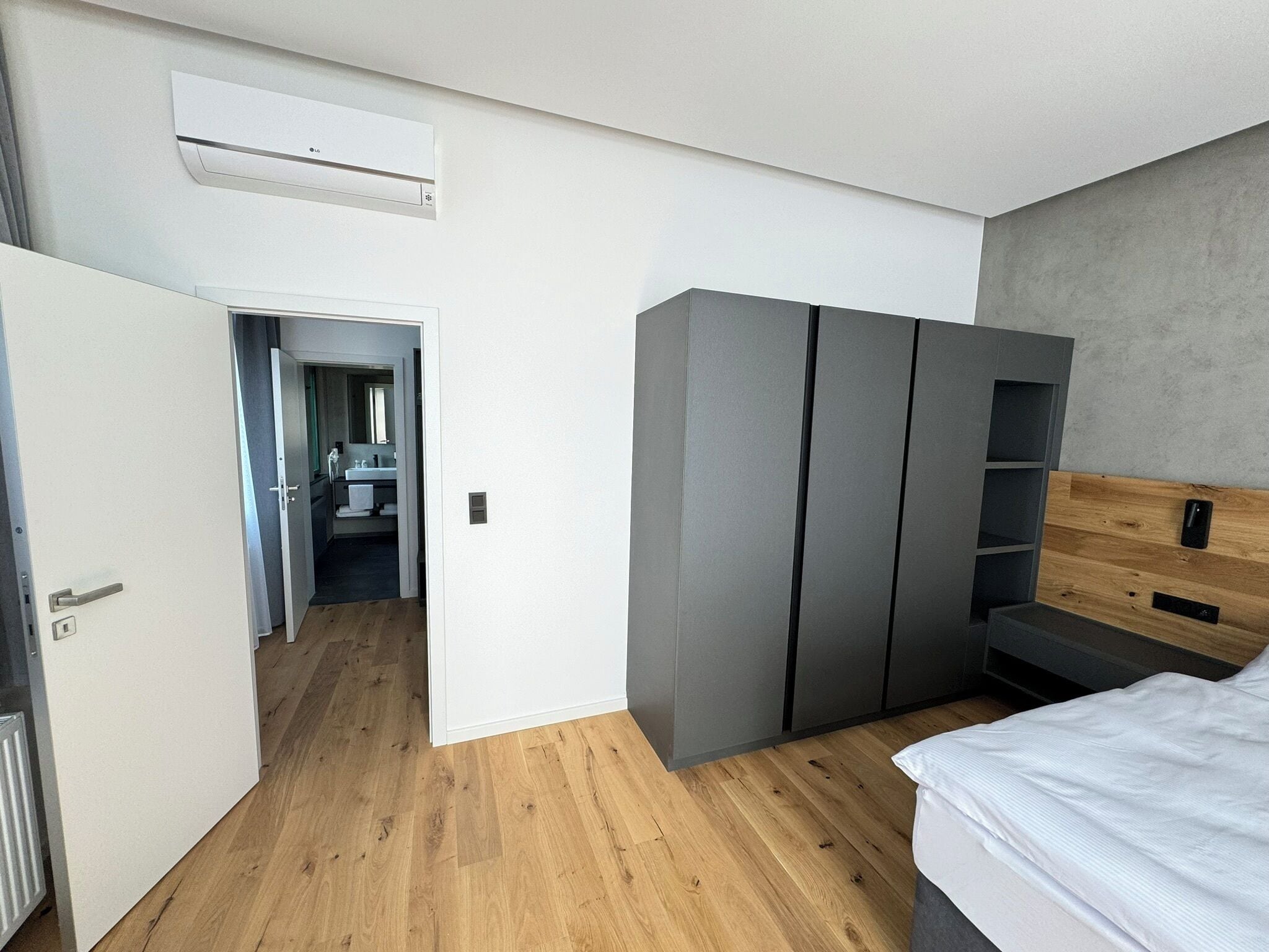A modern bedroom with a bed, grey wardrobe, and a wooden headboard.
