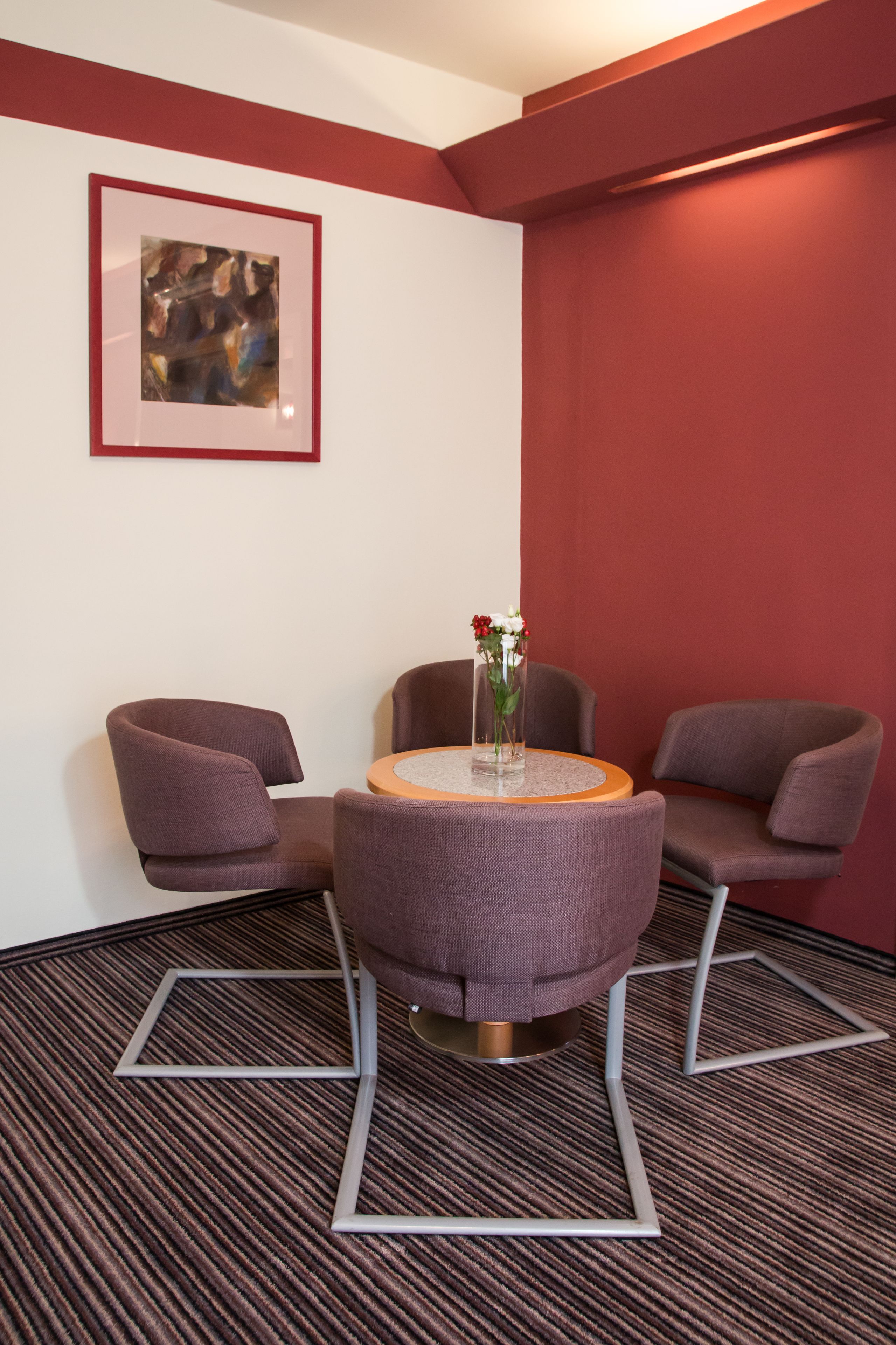 A modern room with a round table, two purple chairs, a framed abstract painting, and a carpeted floor.