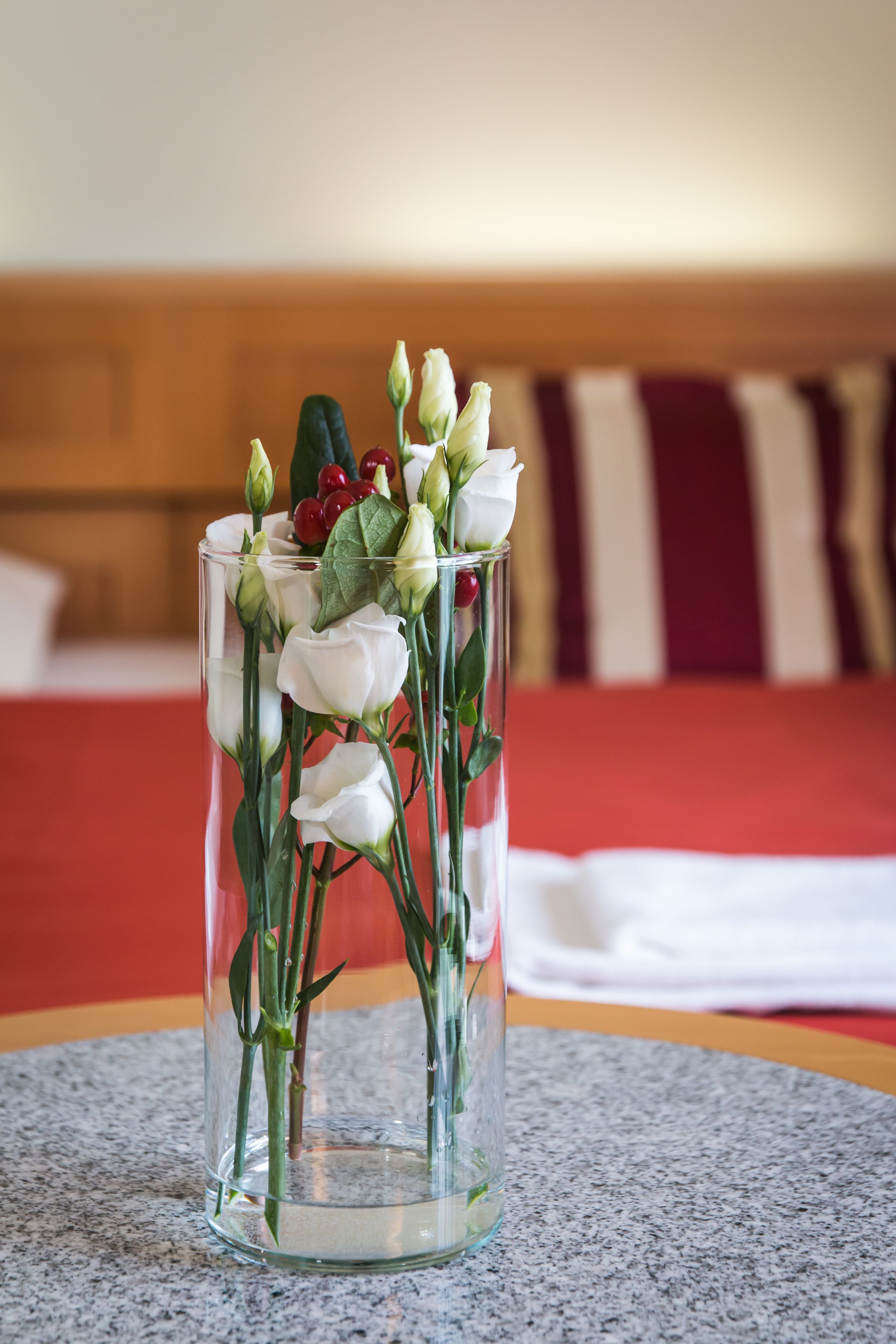 Un florero de vidrio transparente con rosas blancas y hojas verdes sobre una mesa de granito.