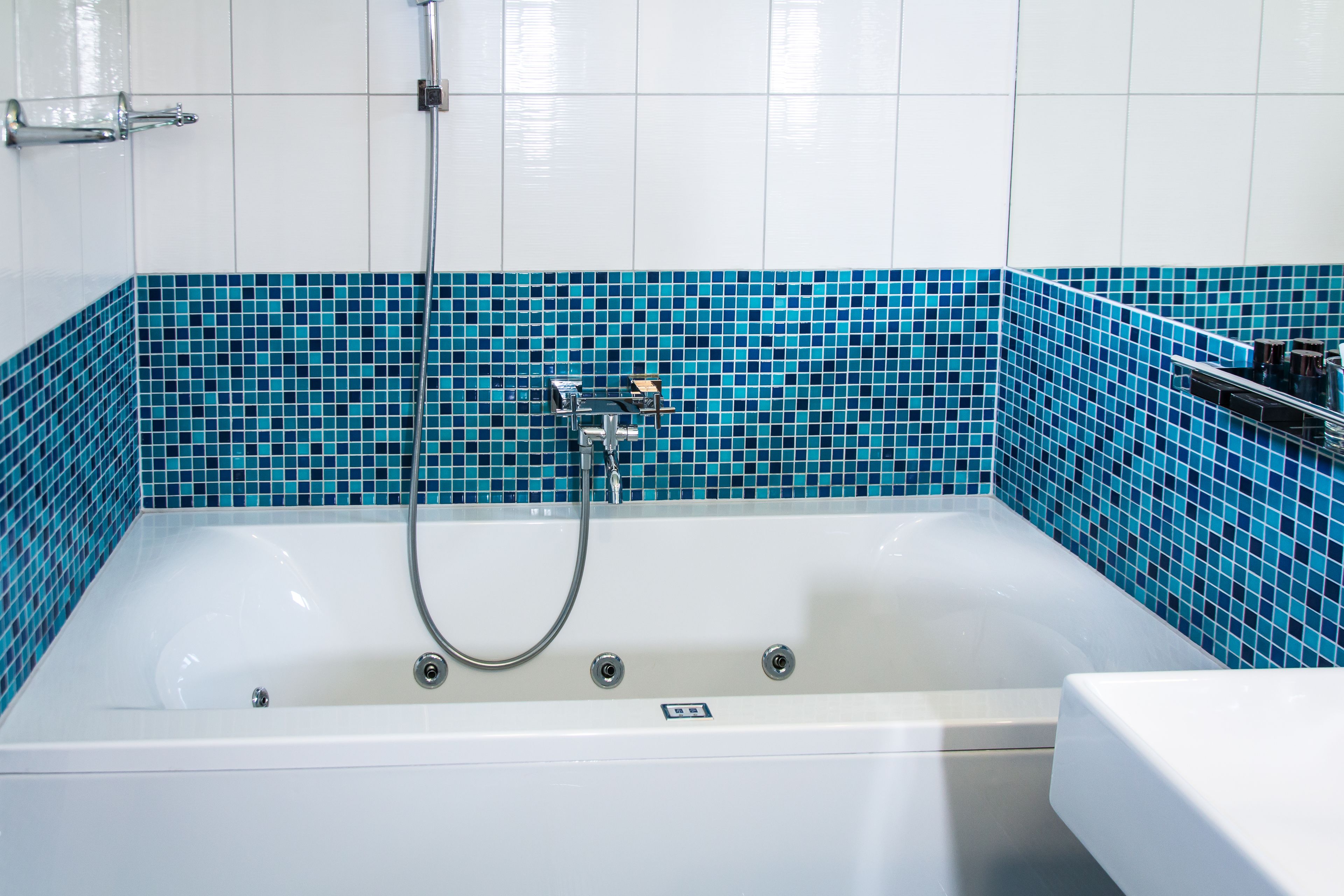 A bathroom with a white bathtub, a showerhead, and a blue-tiled wall.