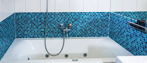 A bathroom with a white bathtub, a showerhead, and a blue-tiled wall.