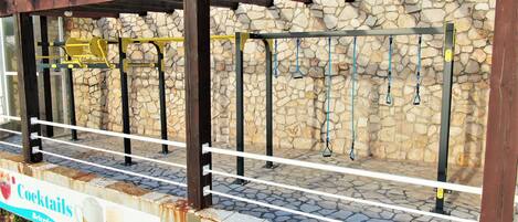 An outdoor gym area with exercise equipment, a stone wall, and a sign advertising cocktails and beer.